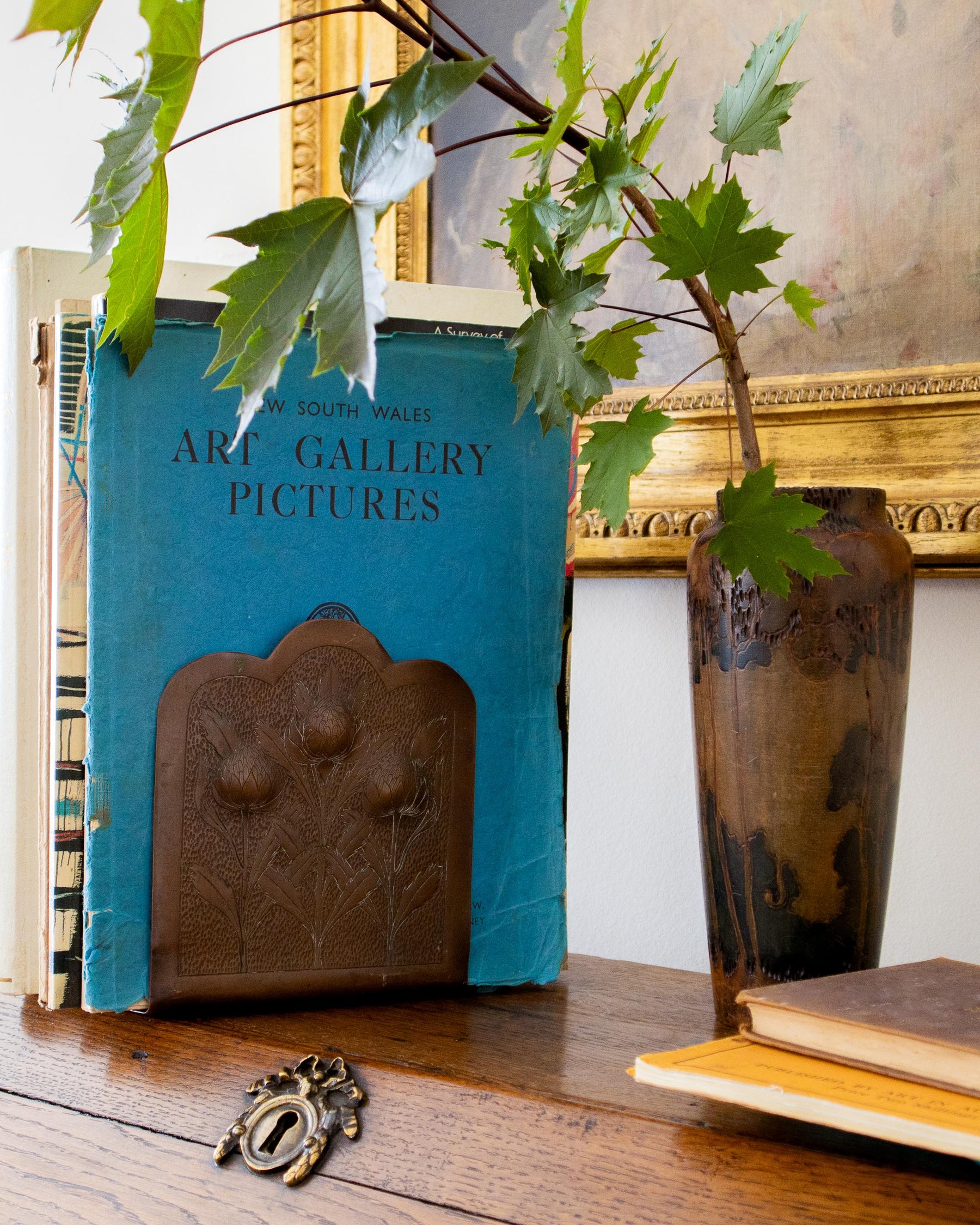 Blue book titled 'Art Gallery Pictures' with a decorative vase and plant on a wooden surface.