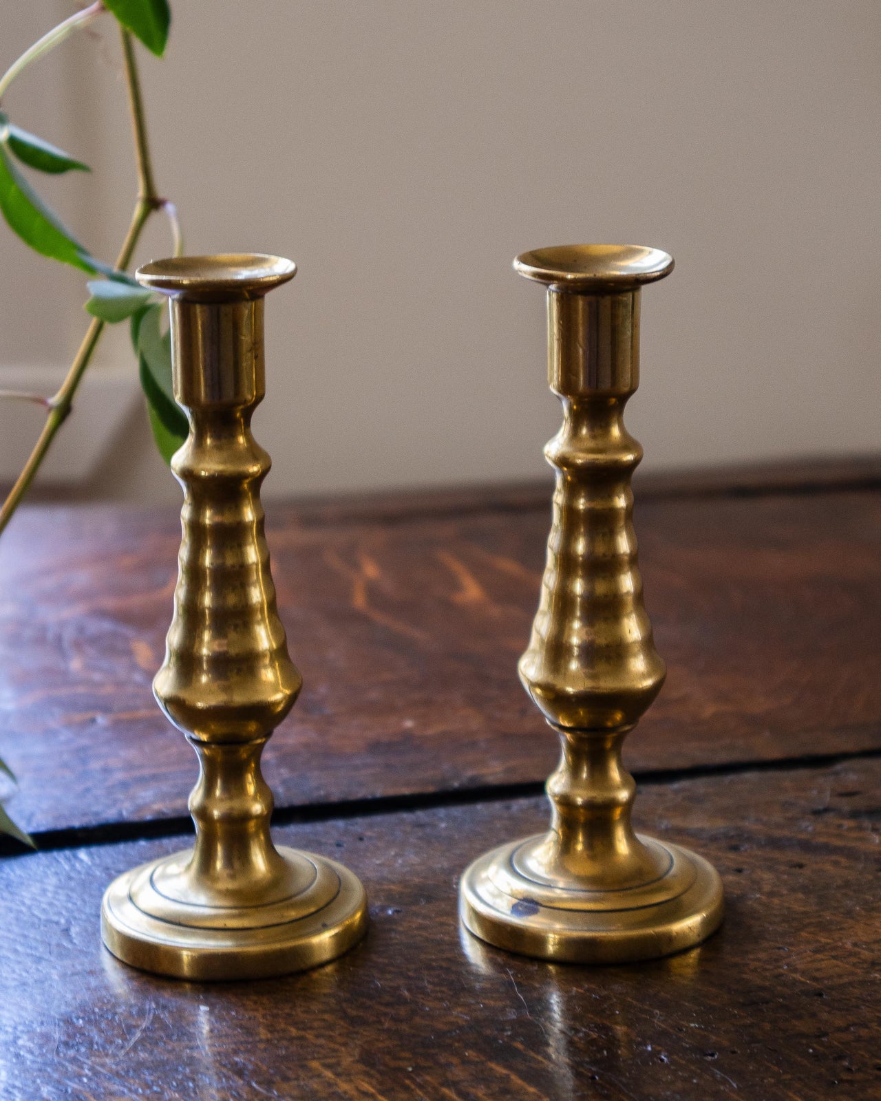 Two brass tapersticks on a wooden surface with a neutral background