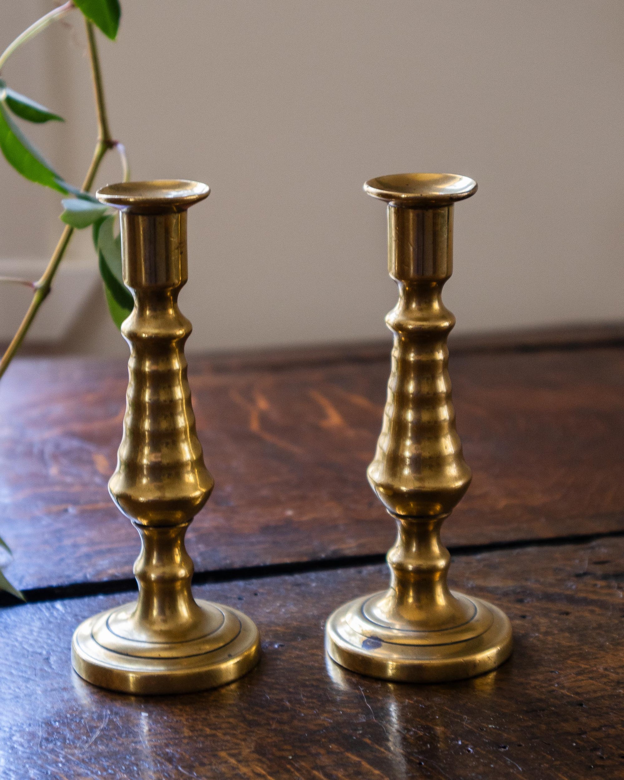 Two brass tapersticks on a wooden surface with a neutral background