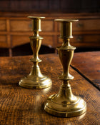Two brass candlesticks on a wooden surface with a wooden background