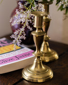Brass candlestick holders with a book and flowers on a wooden surface