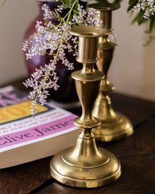 Brass candlestick holders with a book and flowers on a wooden surface
