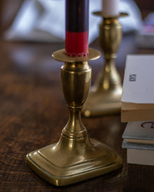 Brass candlestick holder with a red candle on a wooden surface