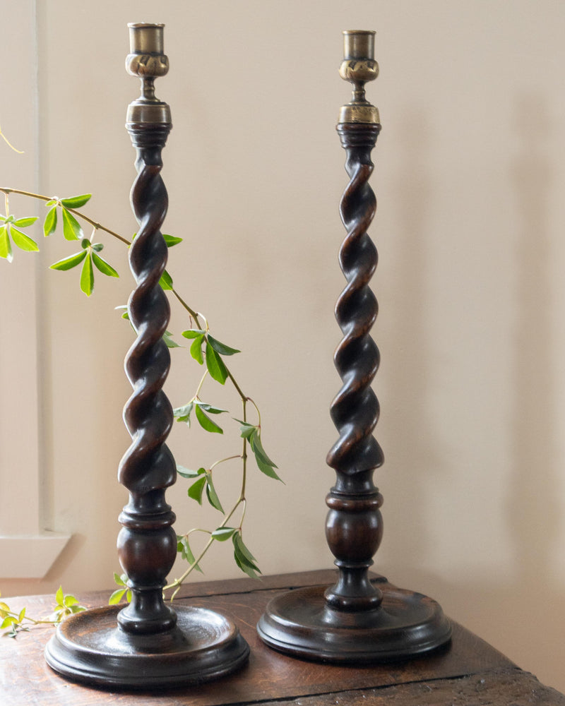 Two twisted wooden candlesticks on a wooden surface with a light background