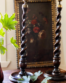 Pair of wooden candlesticks with a decorative painting in the background