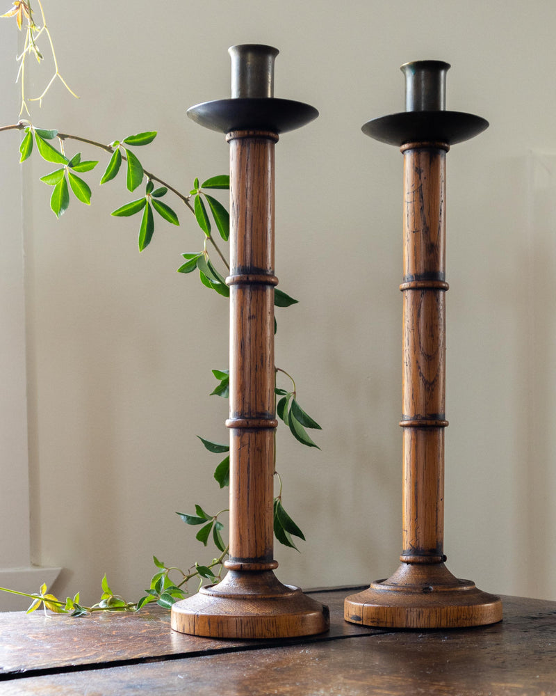 Two wooden candle holders on a table with a plant in the background