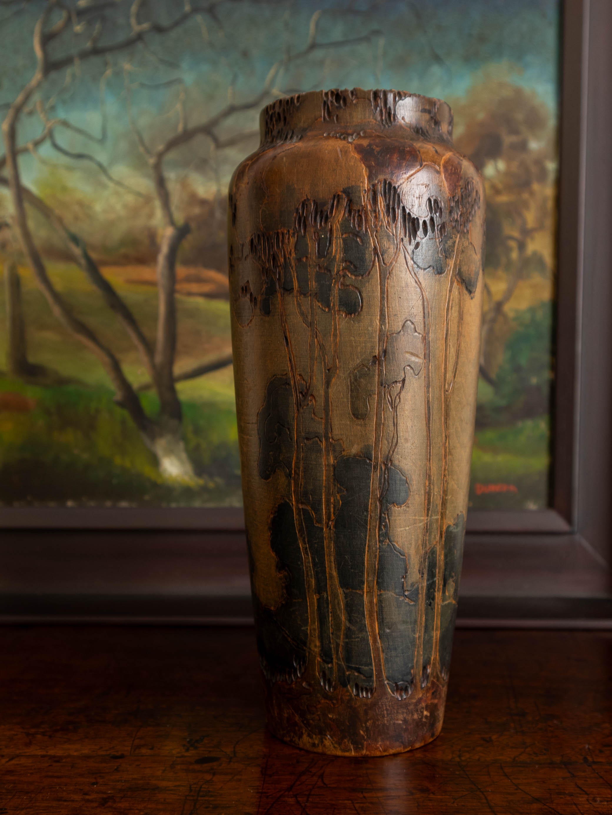 Pokerwork vase with landscape carved surface in front of a landscape painting