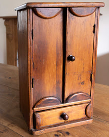 Wooden cabinet with two doors and a drawer on a wooden surface