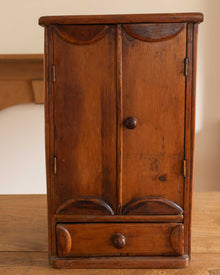 Wooden cabinet with two doors and a drawer on a wooden surface.