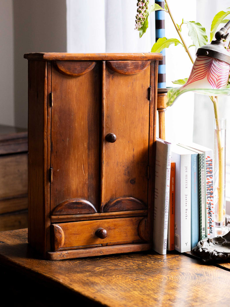 Wooden cabinet on a wooden surface with books and a plant in the background