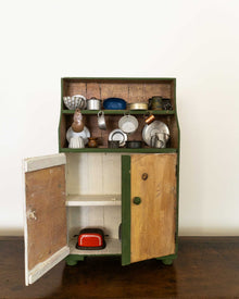 Wooden toy cabinet with open door displaying miniature kitchen items on a white background