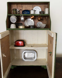 Wooden toy kitchen with shelves containing various toy kitchen items.