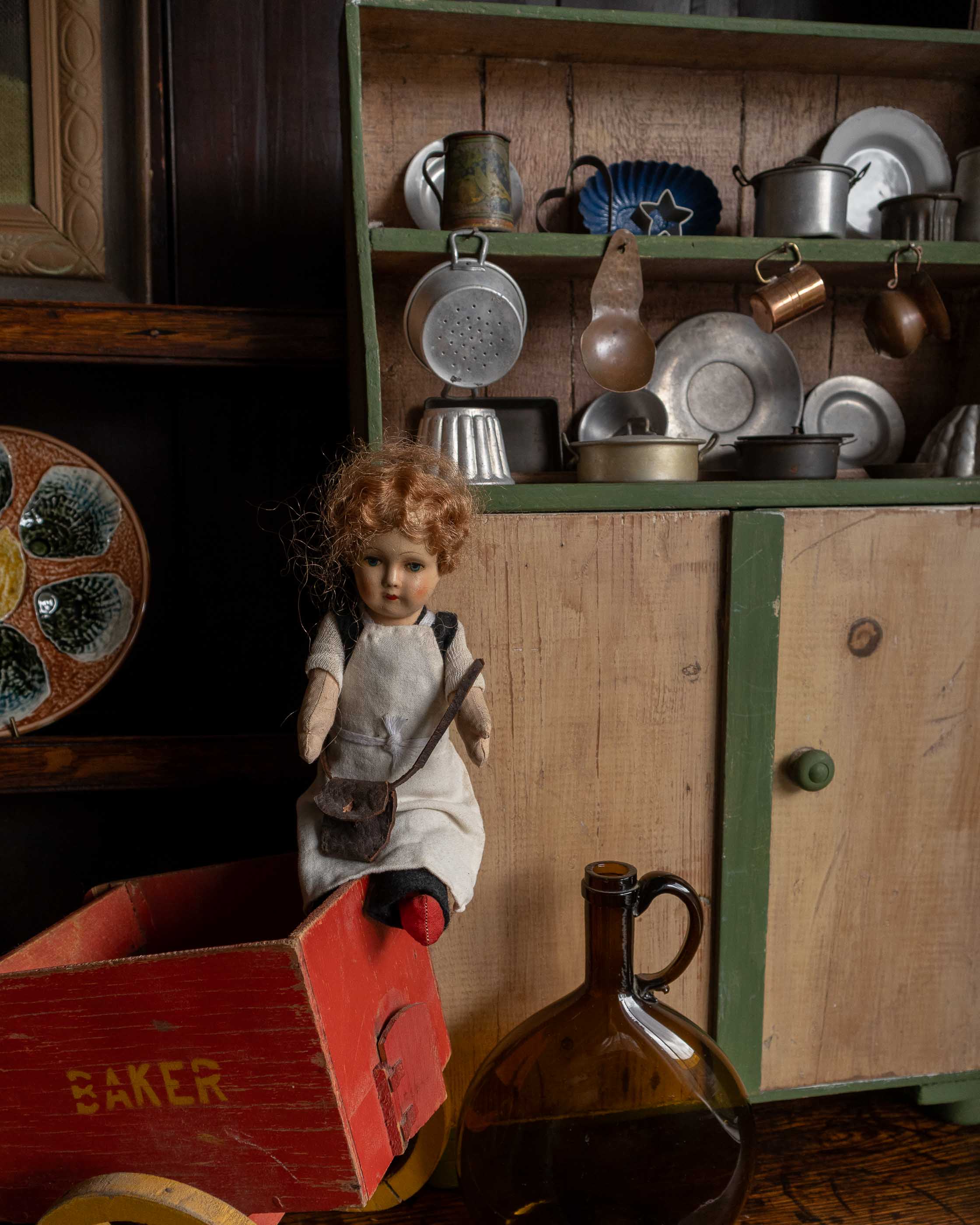 Vintage doll with a red cart and kitchenware in a rustic setting