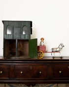 Vintage toy house with a child figurine and horse on a wooden surface.