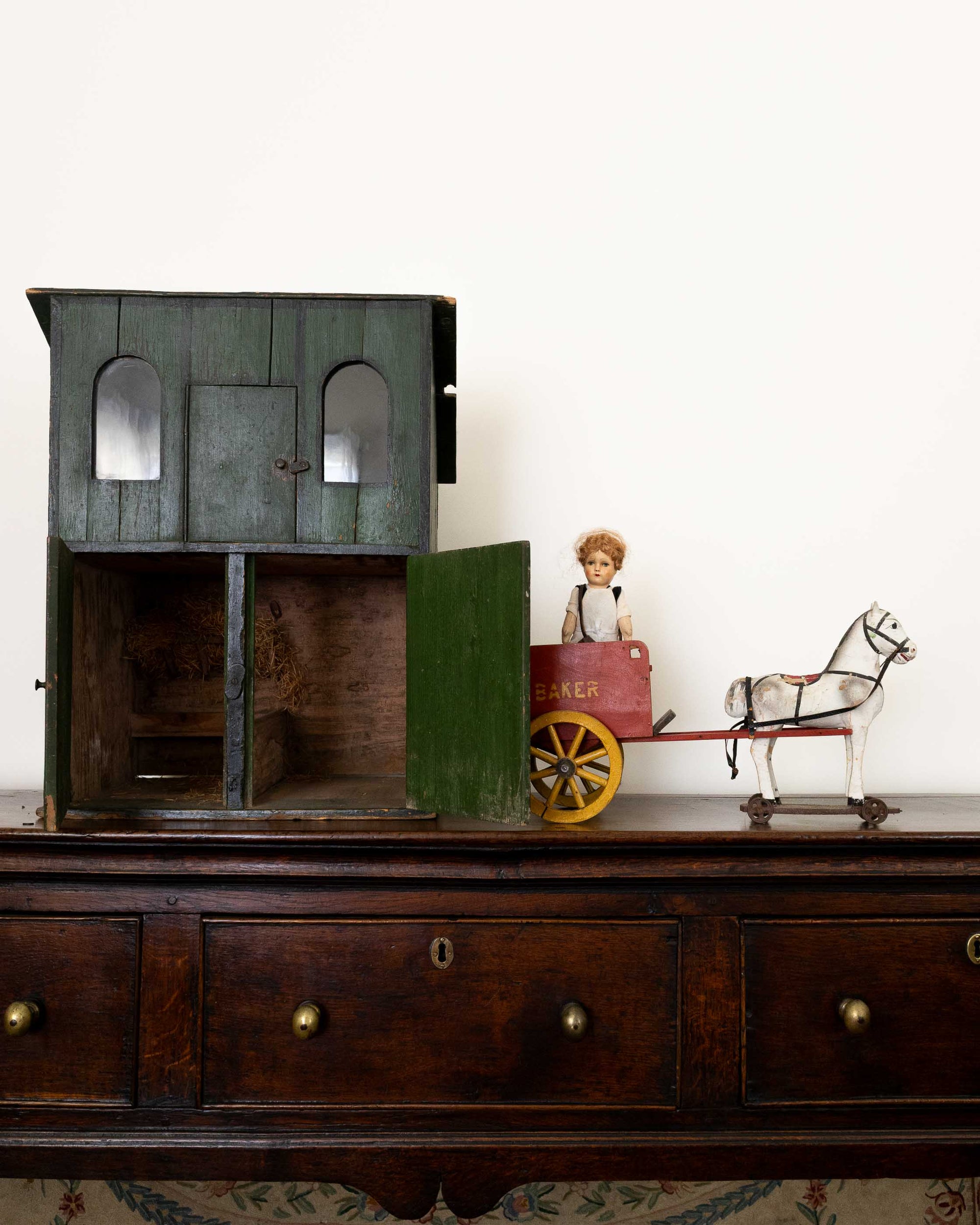 Vintage toy house with a child figurine and horse on a wooden surface.