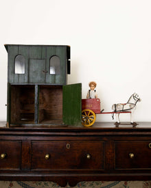 Vintage toy house with a child figurine and horse on a wooden surface.