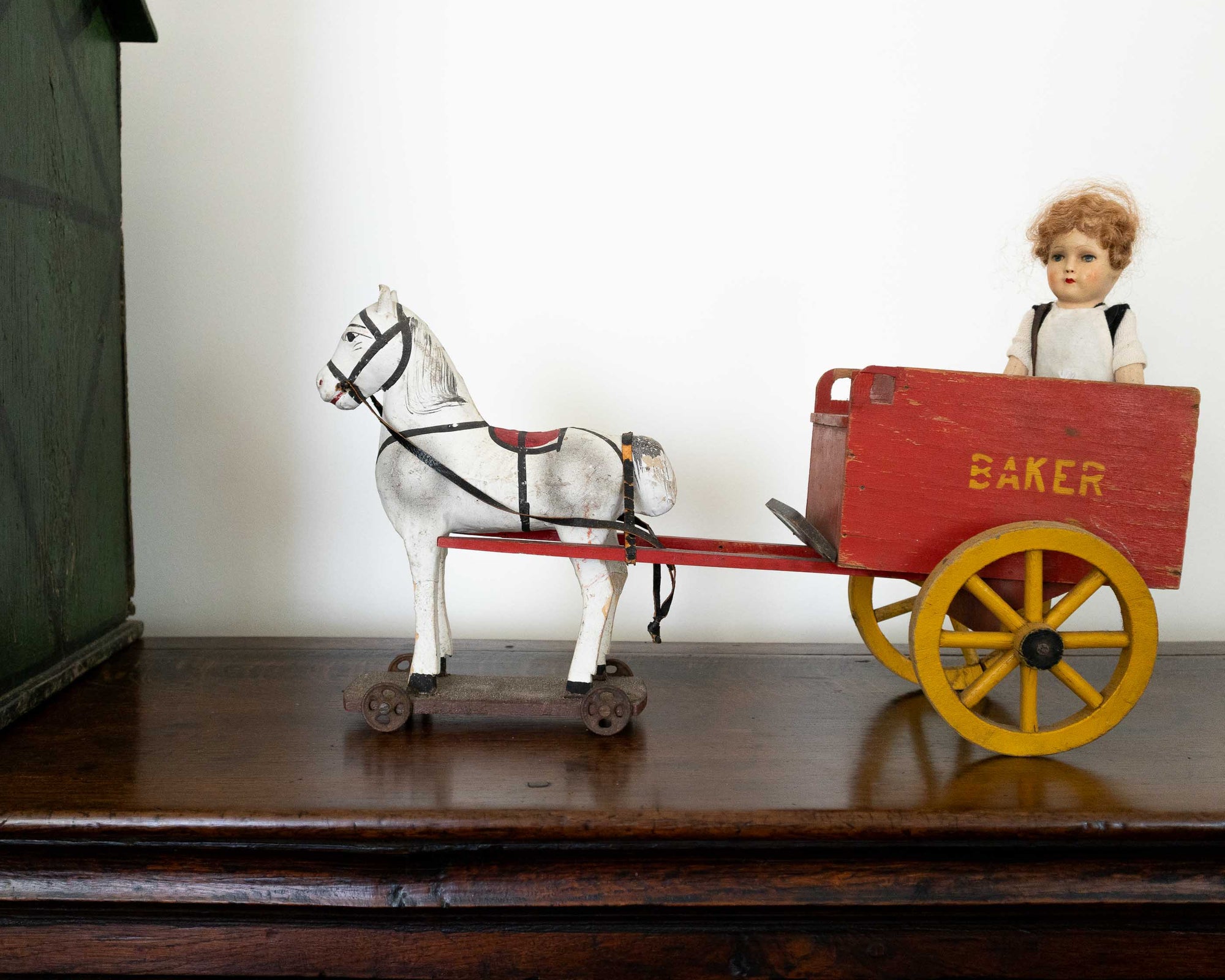 Vintage toy horse pulling a red cart with a doll inside on a wooden surface.