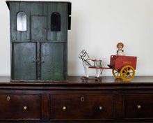 Vintage toy horse and cart on a wooden dresser with a green wooden cabinet in the background.