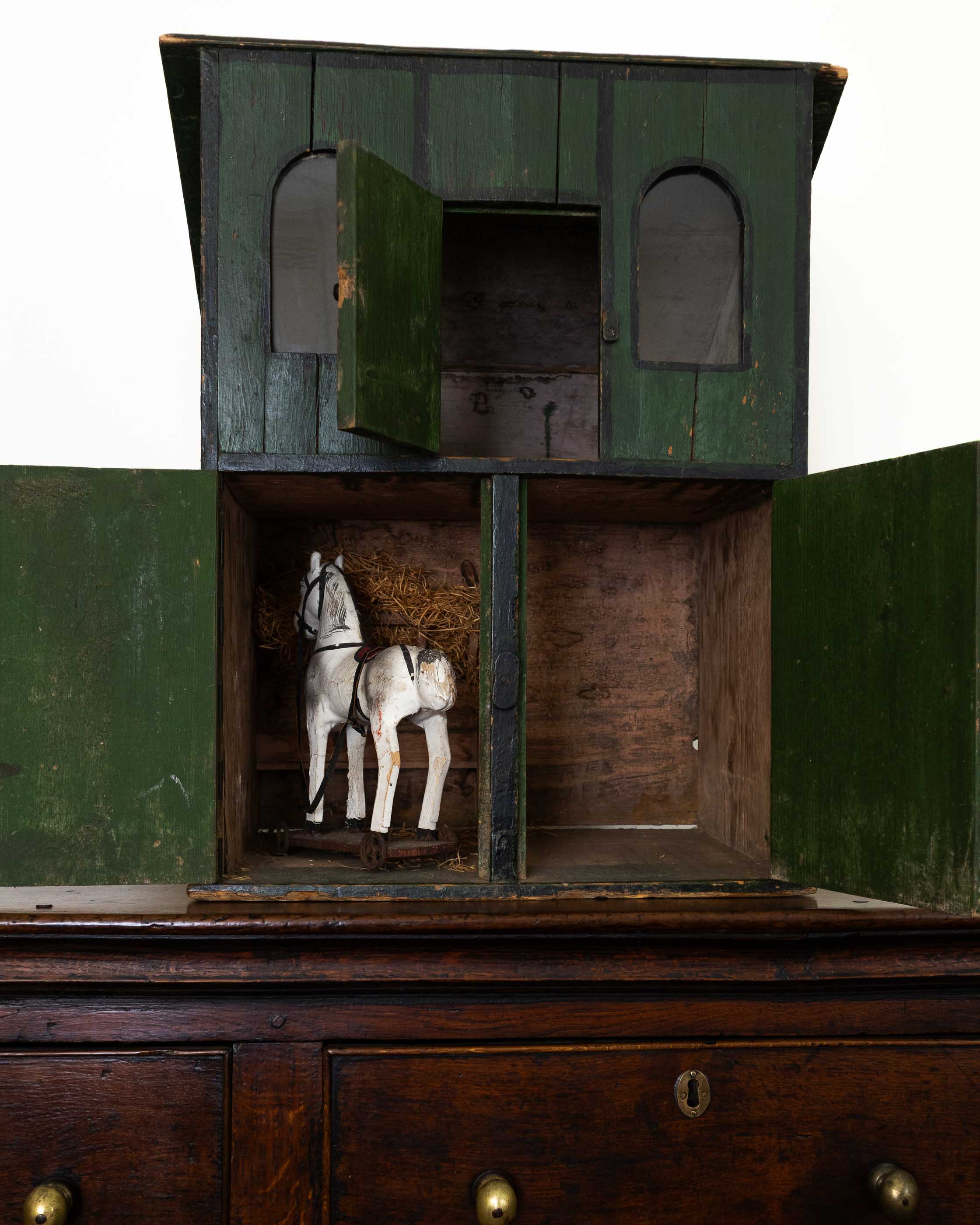 Wooden toy stable with a horse figure inside on a white background
