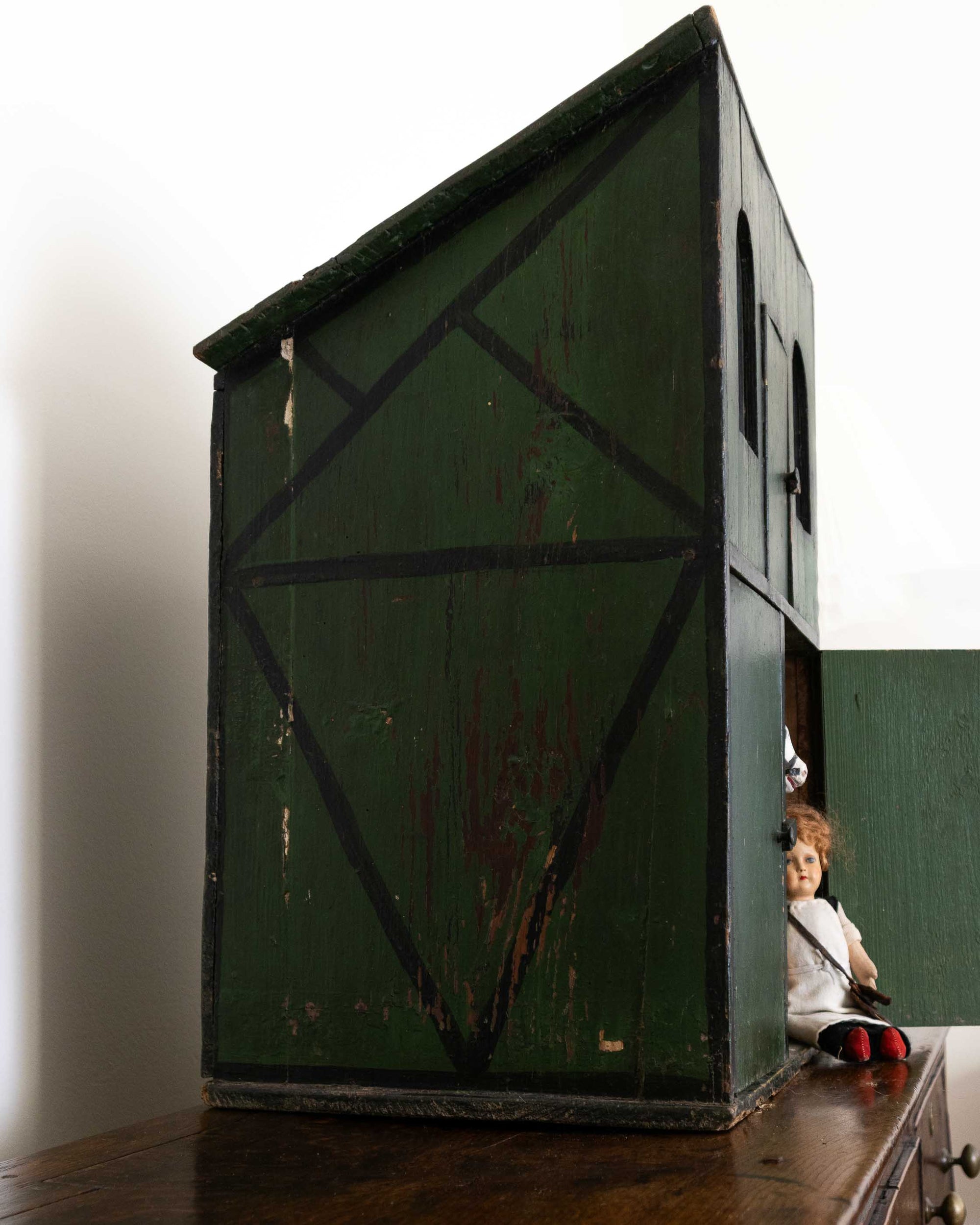 Doll sitting inside a large green wooden box with a white background
