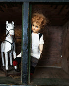 Vintage doll with a white dress and red hair standing behind bars next to a white horse toy.