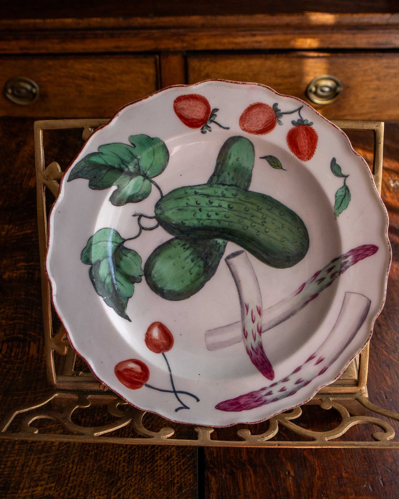 Decorative plate with cucumber, strawberry, and cherry design on a wooden surface.