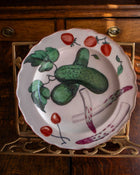 Decorative plate with cucumber, strawberry, and cherry design on a wooden surface.