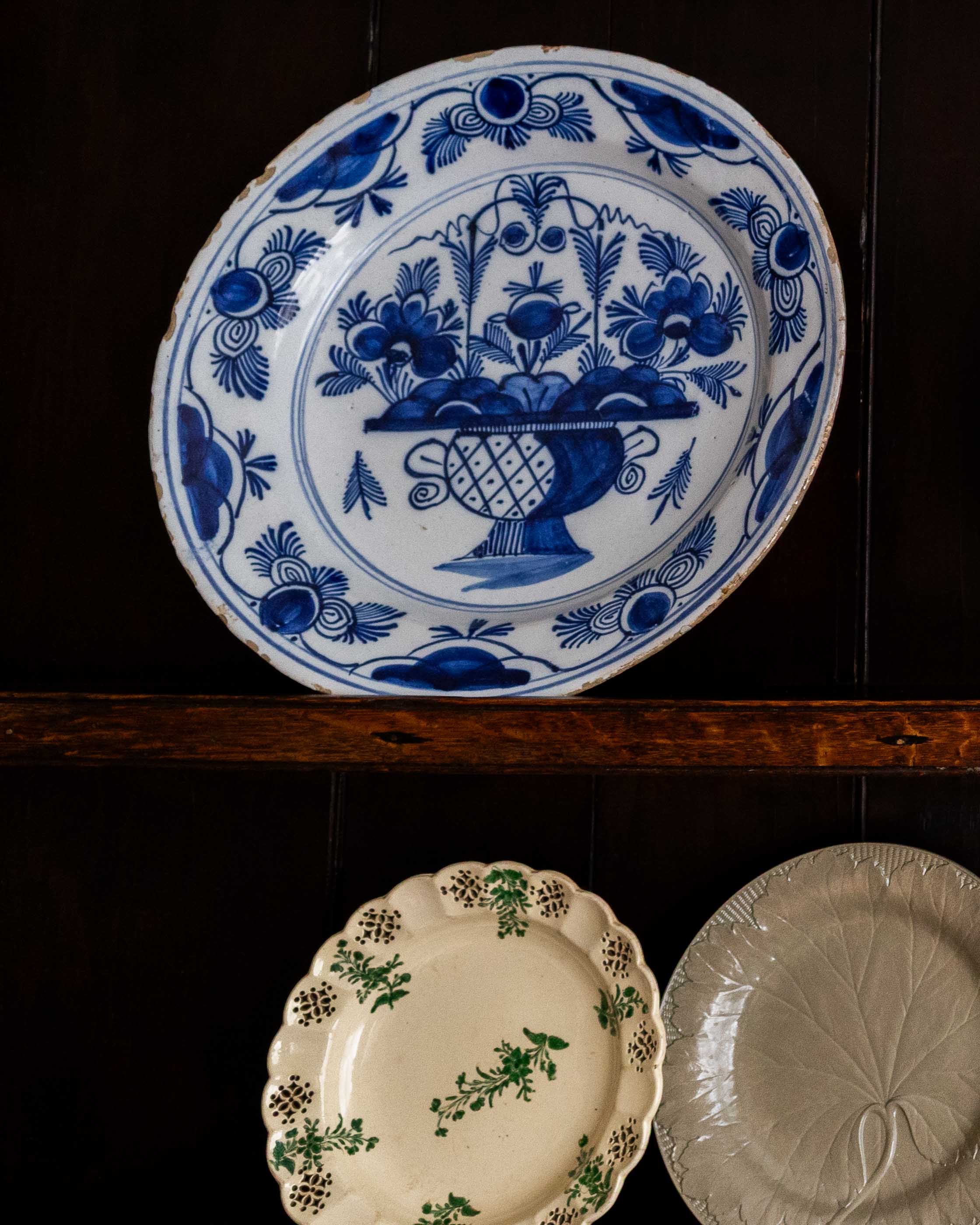 Three ceramic plates with different designs on a dark wooden shelf.