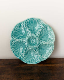 Turquoise ceramic plate with shell design on a wooden surface and white background