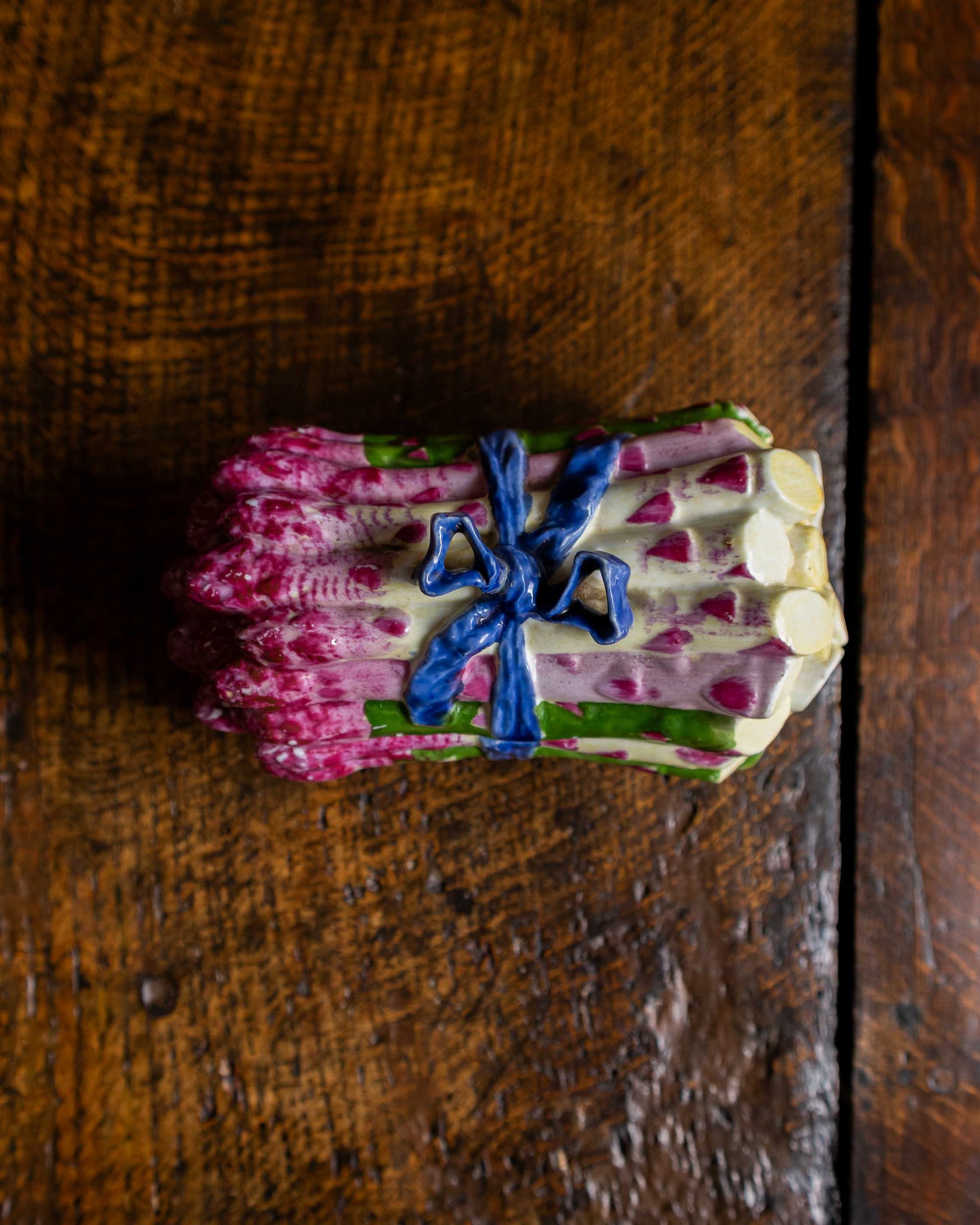 Pink and green and blue ceramic asparagus box on a wooden surface