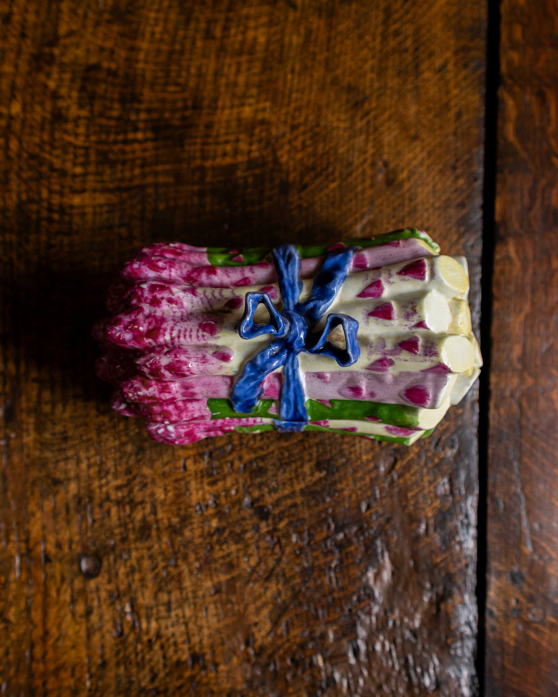 Pink and green and blue ceramic asparagus box on a wooden surface