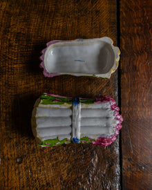 Pink and green and blue ceramic asparagus box on a wooden surface