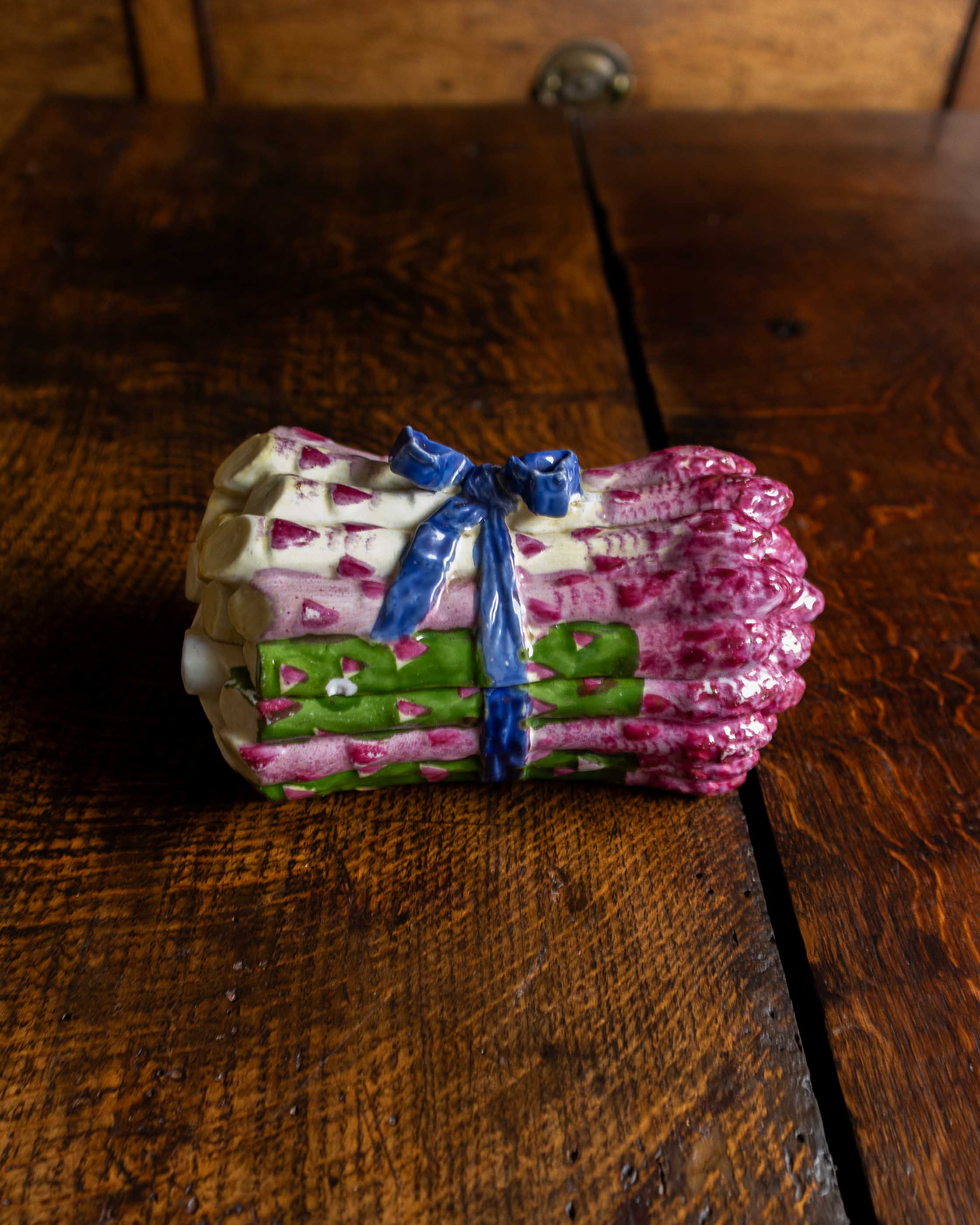 Pink and green and blue ceramic asparagus box on a wooden surface