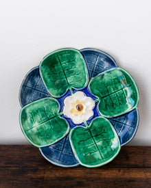 Ceramic plate with green leaf-like shapes and a white center on a wooden surface.