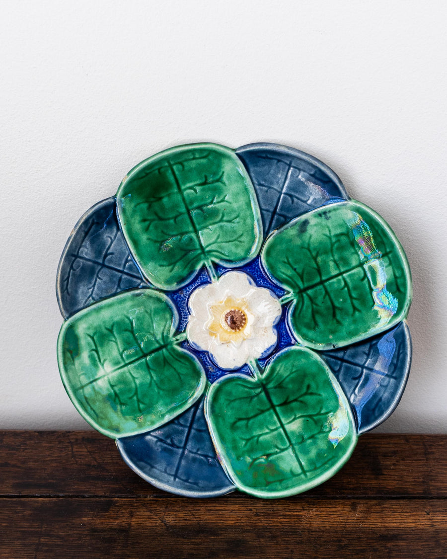 Antique majolica plate with green leaf-like shapes with a white flower center by Griffen, Smith & Hill on a wooden surface.