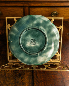 Green ceramic plate with a logo on a decorative stand against a wooden background