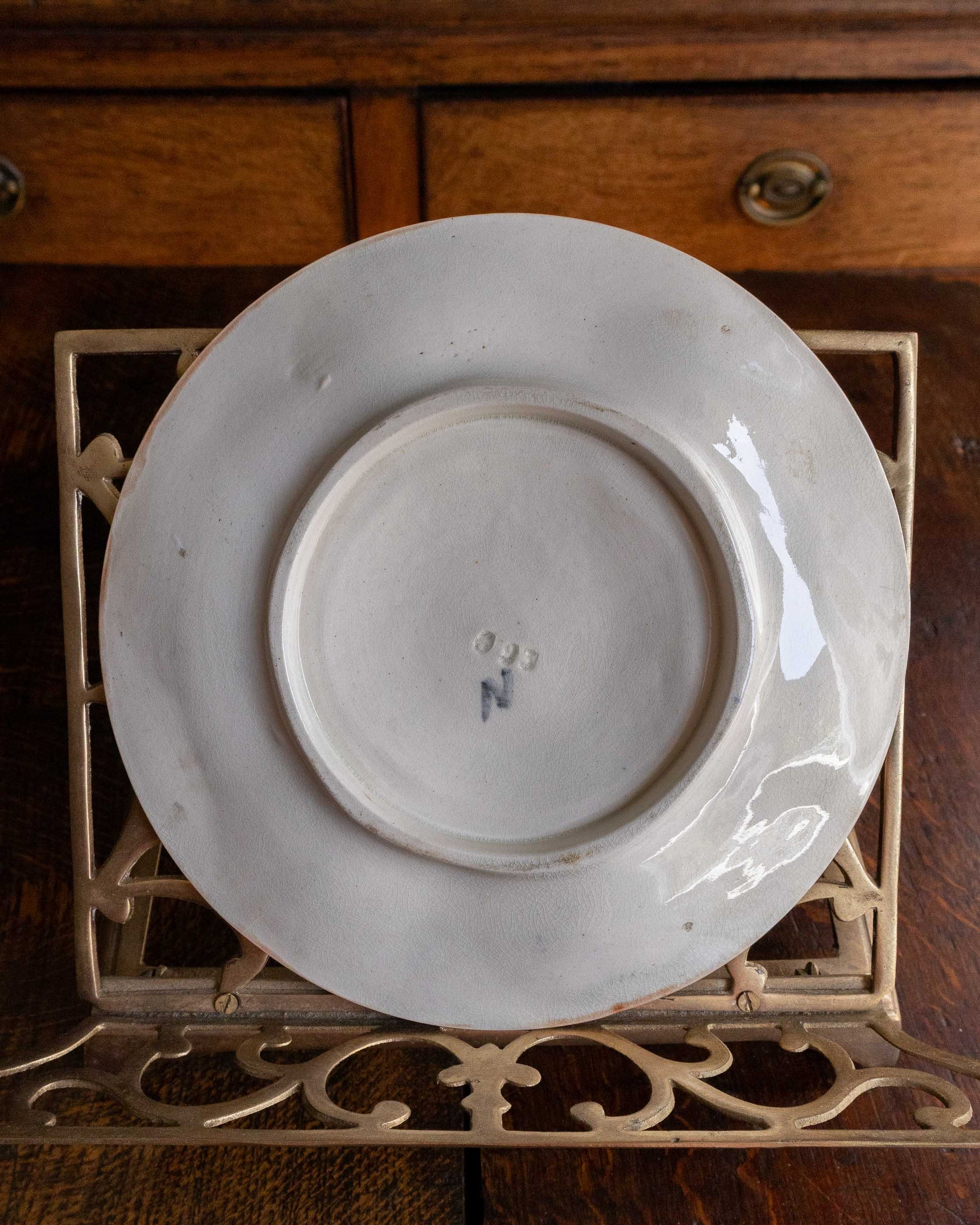 White ceramic plate on a decorative metal stand with wooden cabinet in the background