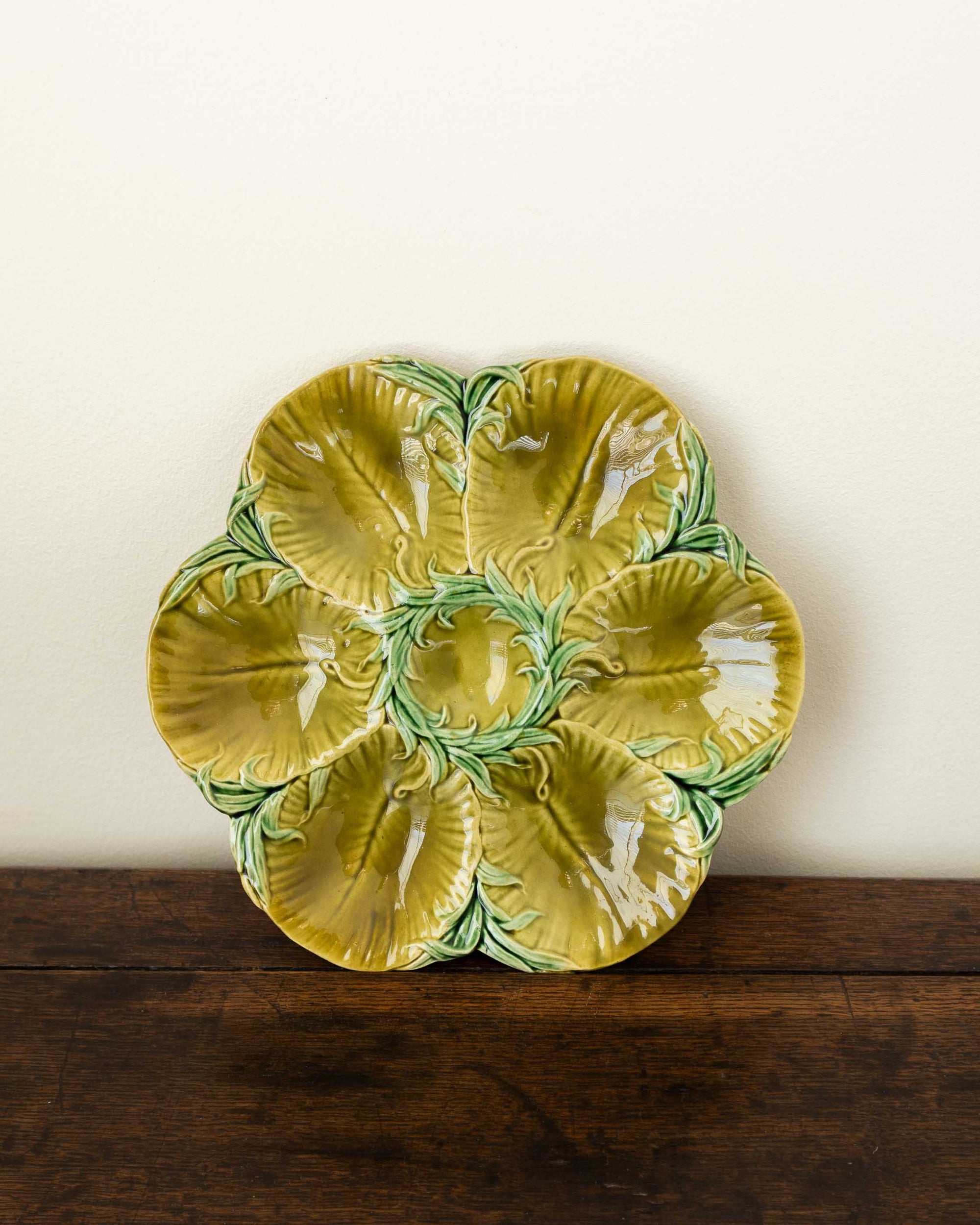 Decorative green oyster plate with green shell patterns on a wooden surface and white wall background