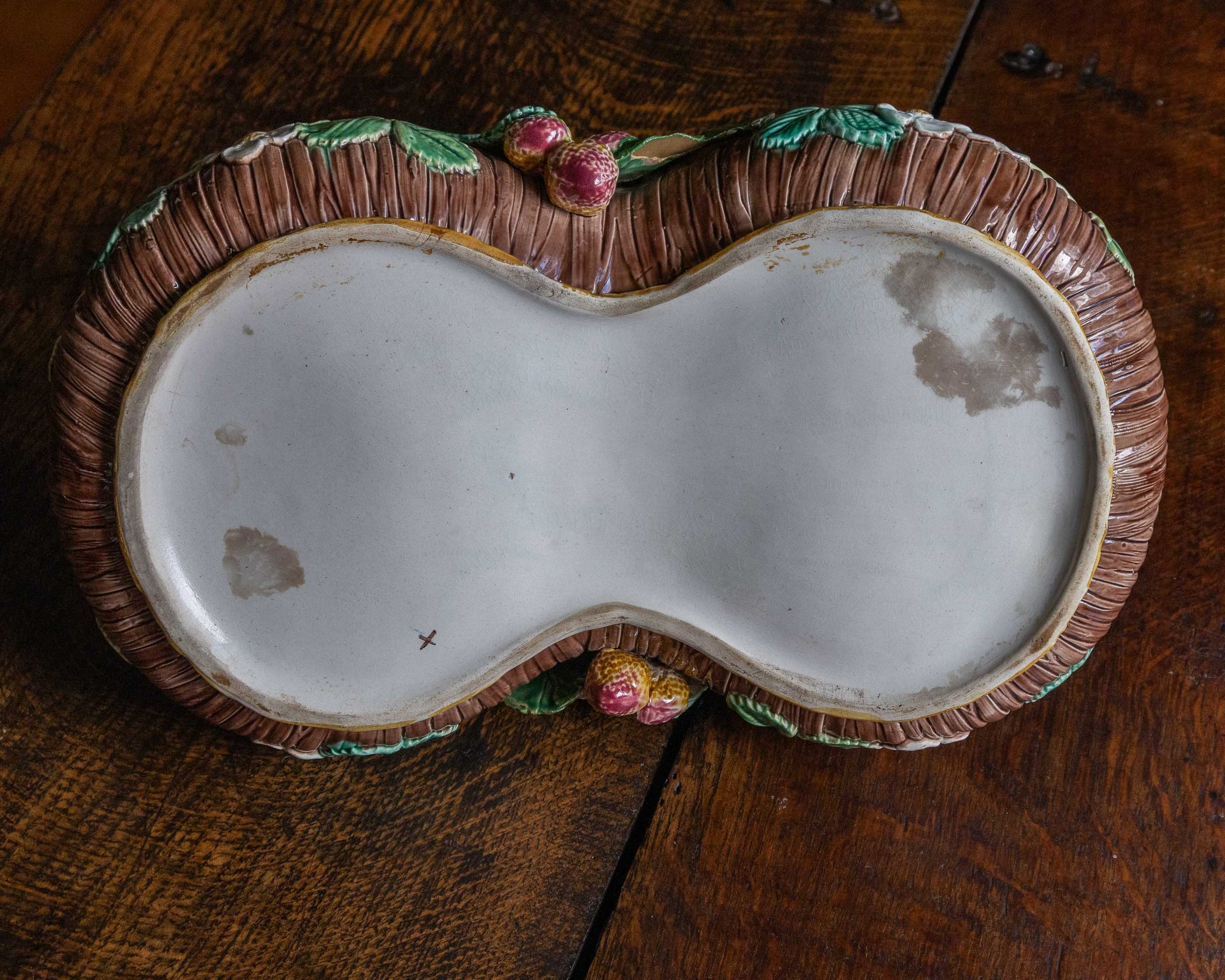 Base of majolica strawberry basket on a wooden surface
