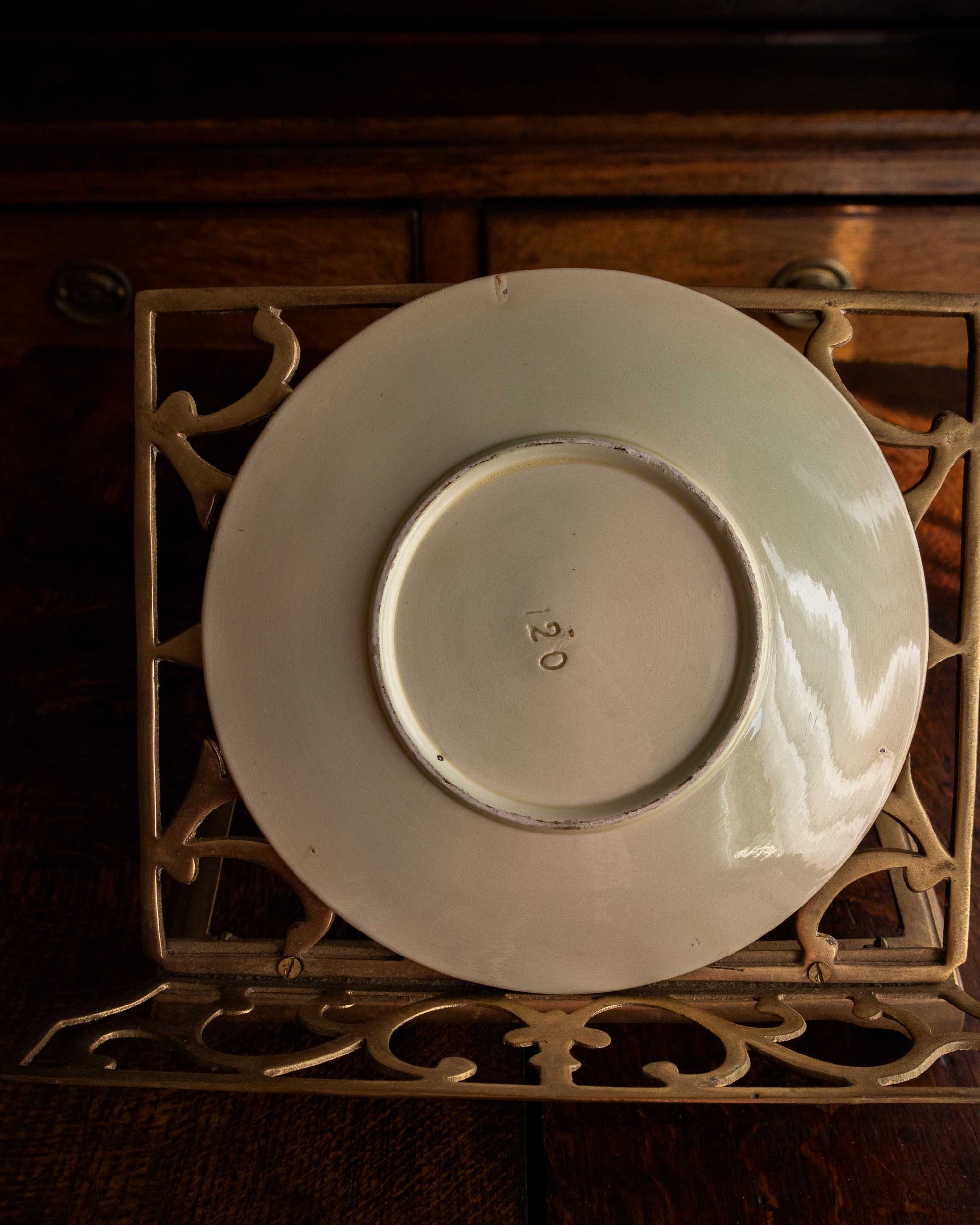 White ceramic plate with '120' on a decorative metal stand against a wooden background