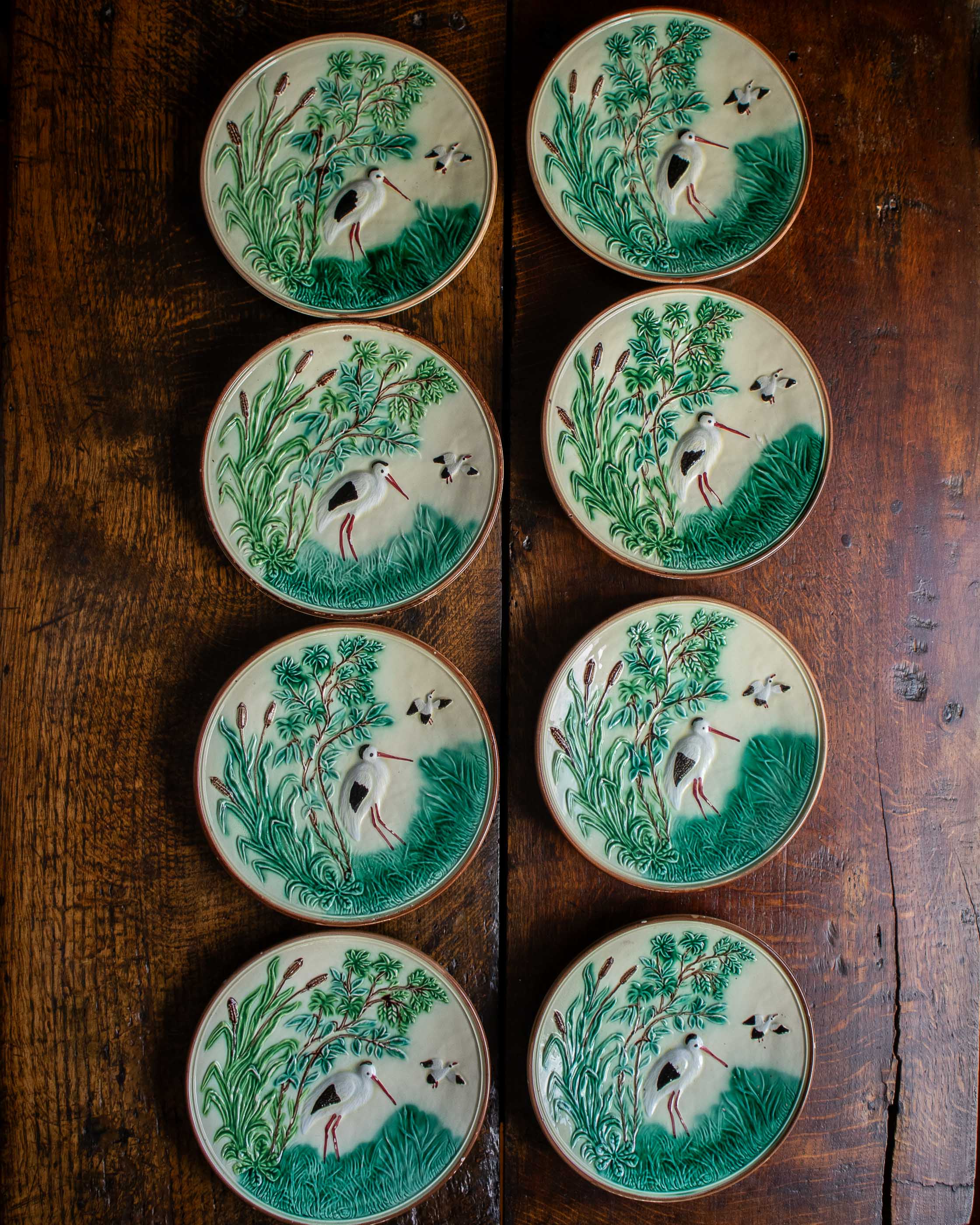 Set of eight ceramic plates with nature-themed designs on a wooden surface