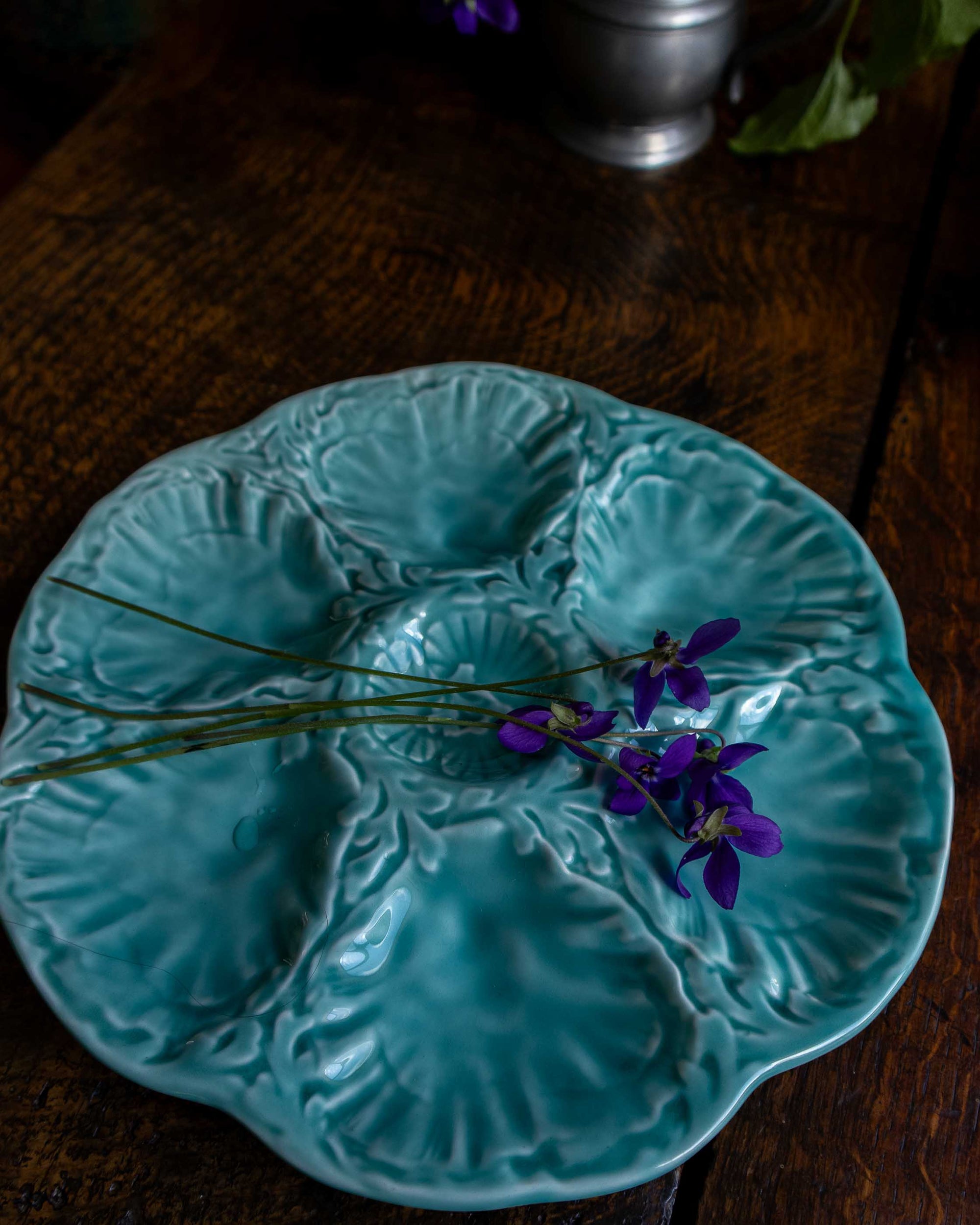 Turquoise ceramic majolica oyster plate with floral arrangement on a wooden surface