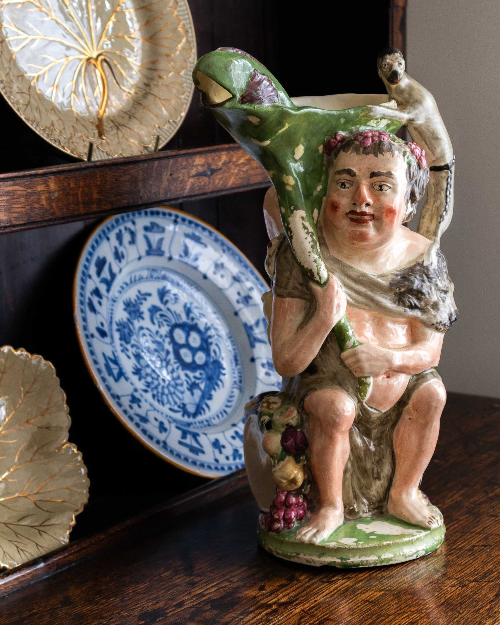 Decorative ceramic figure of a bacchus with flowers on a wooden surface.