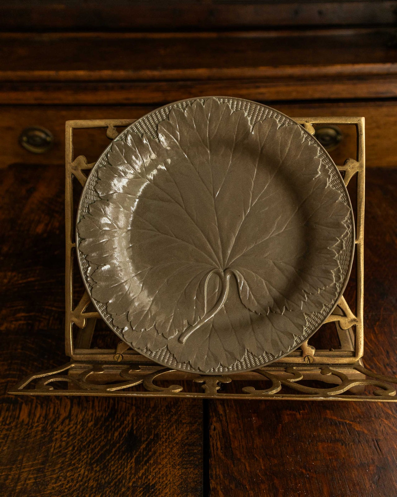 Decorative plate with leaf design on a metal stand against a wooden background