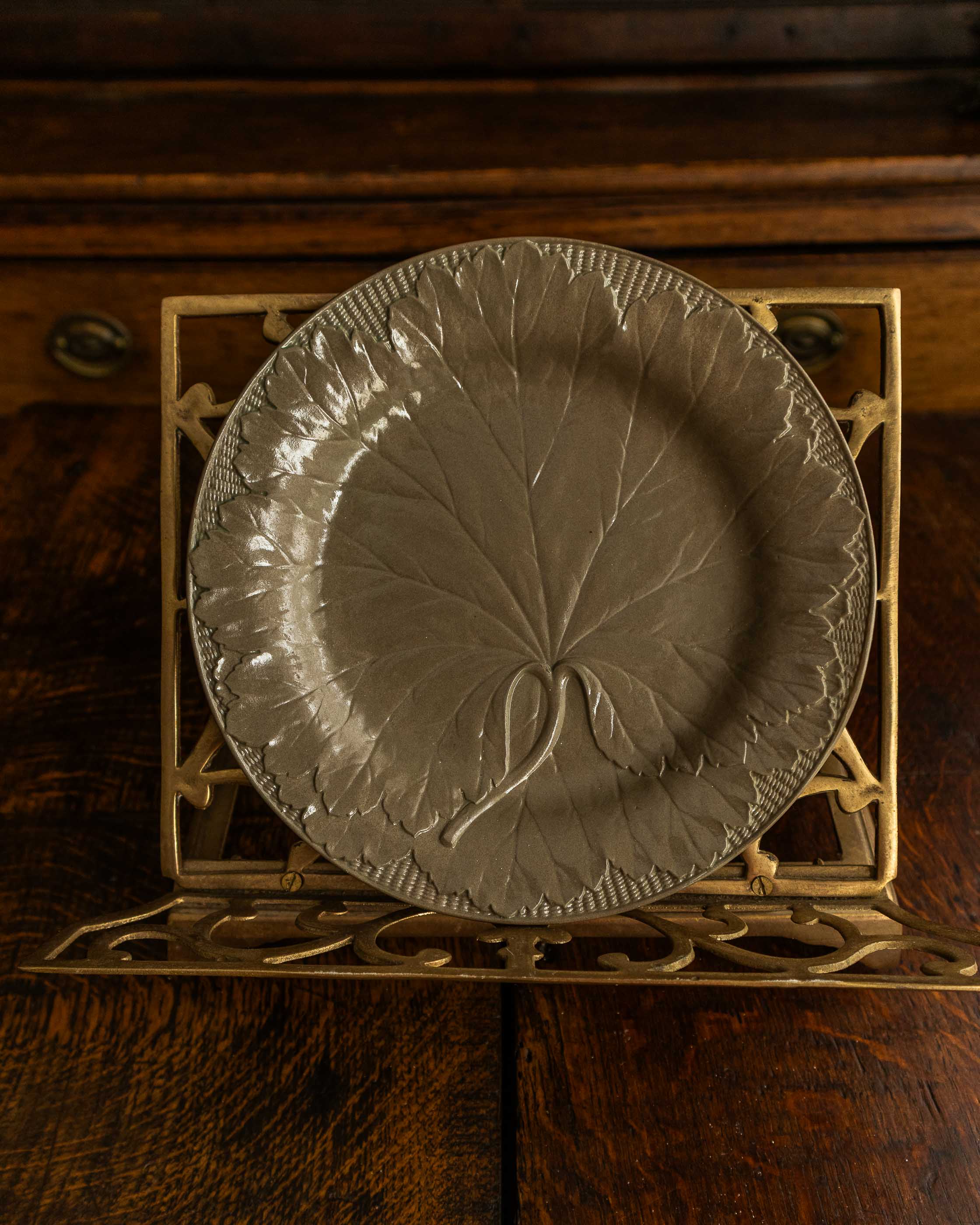 Decorative plate with leaf design on a metal stand against a wooden background