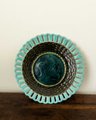 Decorative ceramic plate with turquoise rim and black interior on a wooden surface.