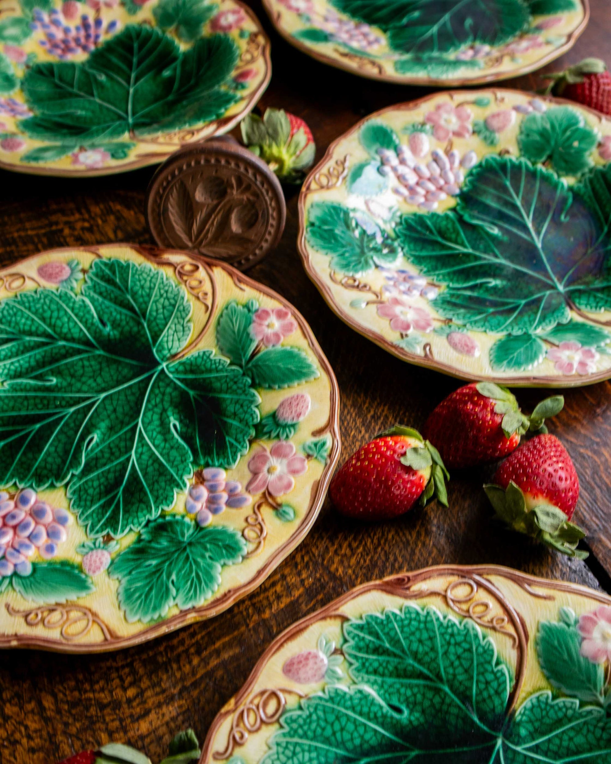 Decorative plates with leaf and strawberry designs on a wooden surface.