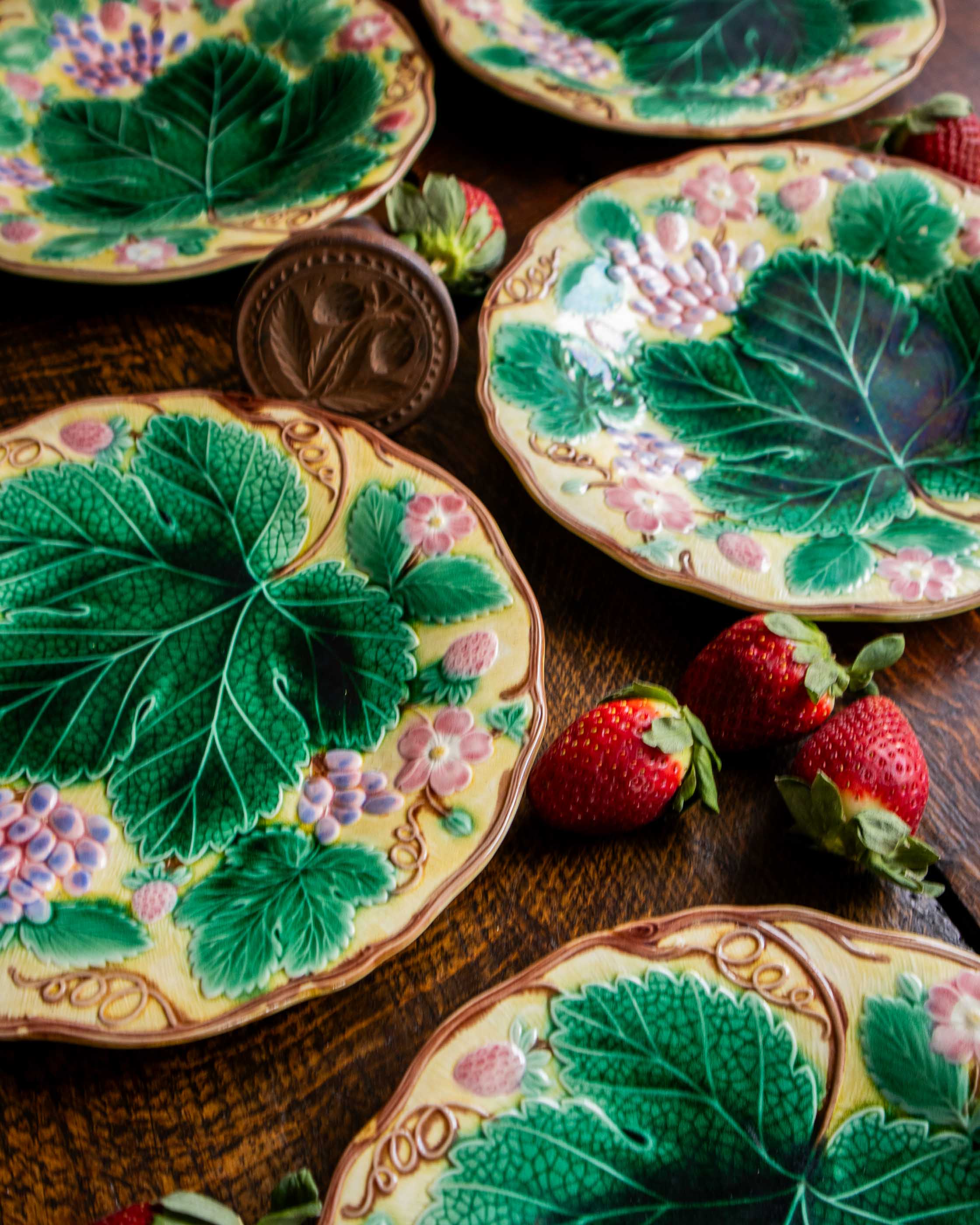 Decorative plates with leaf and strawberry designs on a wooden surface.
