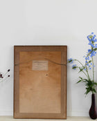 Wooden picture frame with a label on a white wall next to a vase with flowers