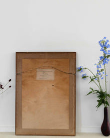 Wooden picture frame with a label on a white wall next to a vase with flowers
